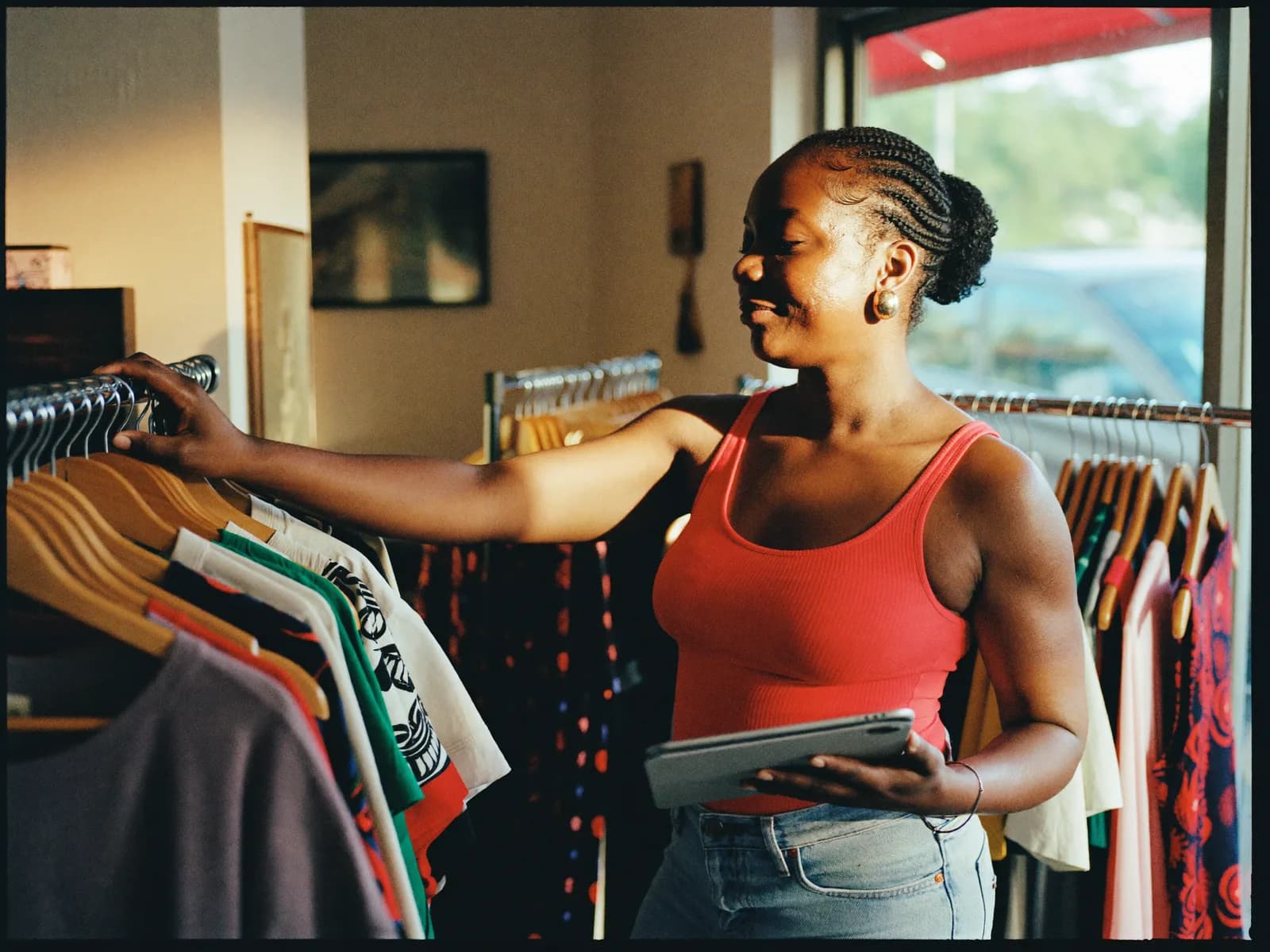 Propriétaire de boutique avec sa tablette parmi les portants de vêtements